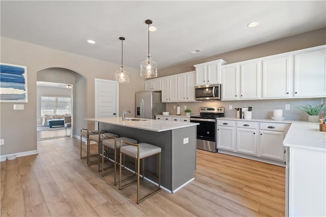 kitchen featuring appliances with stainless steel finishes, light hardwood / wood-style flooring, white cabinets, and an island with sink