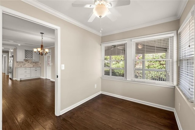 empty room with dark wood finished floors, ceiling fan with notable chandelier, baseboards, and ornamental molding