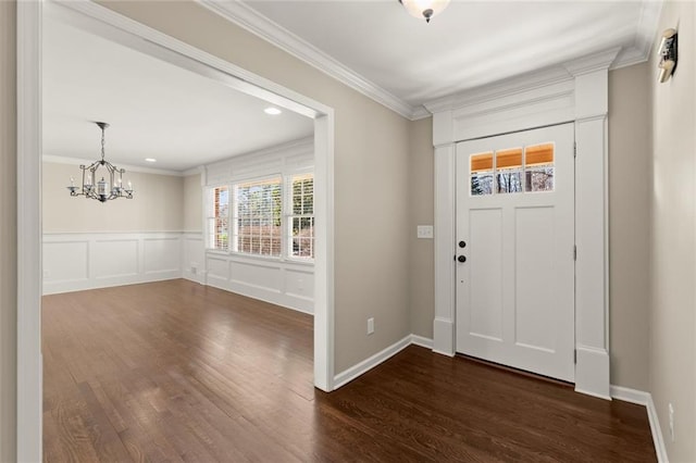 foyer entrance featuring ornamental molding, dark wood-type flooring, wainscoting, a decorative wall, and a notable chandelier