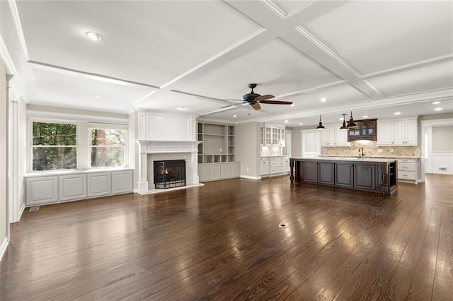 unfurnished living room with dark wood-style floors, a glass covered fireplace, coffered ceiling, a ceiling fan, and a sink