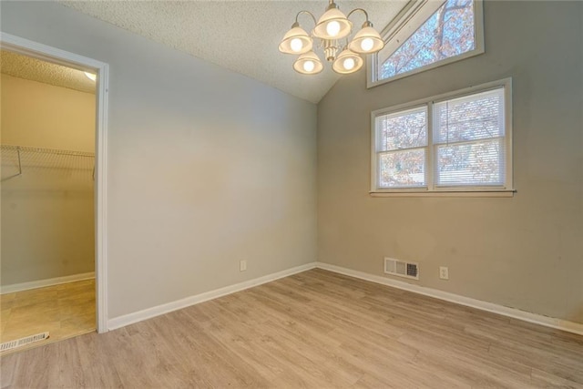 spare room with a textured ceiling, a chandelier, wood-type flooring, and vaulted ceiling