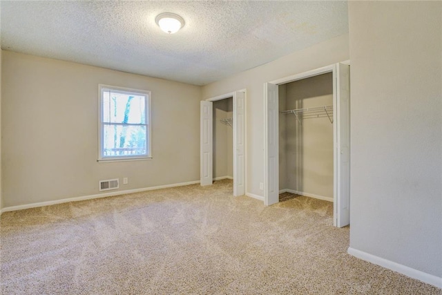 unfurnished bedroom with light carpet, a textured ceiling, and two closets