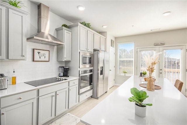 110 Cobalt Dr, Fayetteville, GA 30214 - kitchen featuring light hardwood / wood-style flooring, gray cabinets, appliances with stainless steel finishes, decorative backsplash, and wall chimney exhaust hood
