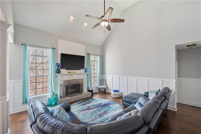 living area with a wainscoted wall, a brick fireplace, a ceiling fan, and wood finished floors