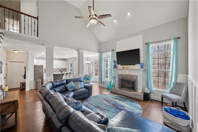 living room featuring a ceiling fan, ornate columns, a fireplace, hardwood / wood-style flooring, and wainscoting