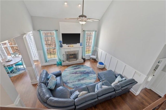 living room featuring a wainscoted wall, a fireplace with raised hearth, high vaulted ceiling, and wood finished floors