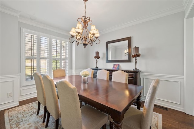 dining space featuring ornamental molding, wood finished floors, wainscoting, and a chandelier