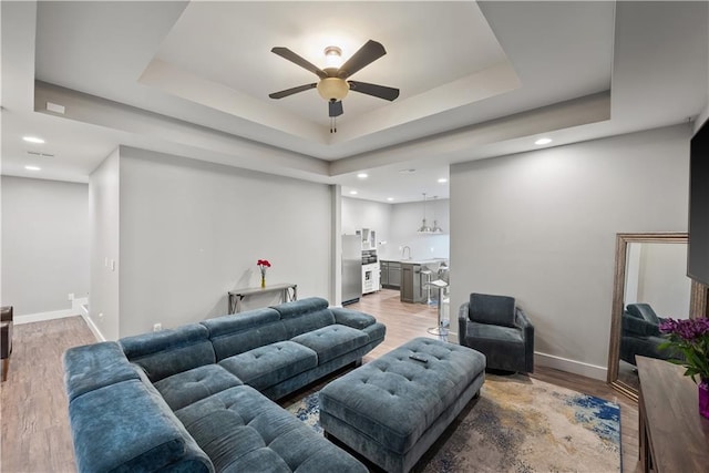 living room featuring baseboards, a raised ceiling, ceiling fan, and light wood finished floors