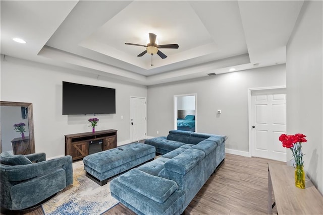 living room featuring light wood finished floors, ceiling fan, baseboards, and a tray ceiling