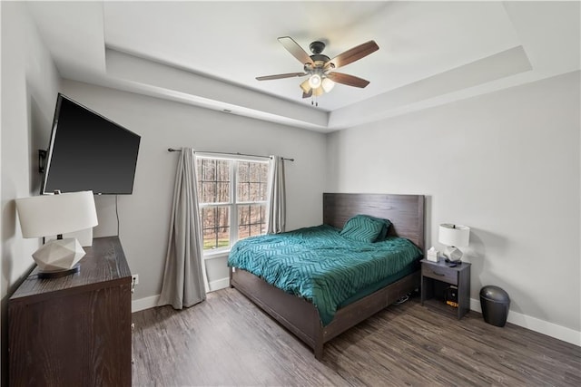 bedroom with baseboards, a raised ceiling, and wood finished floors