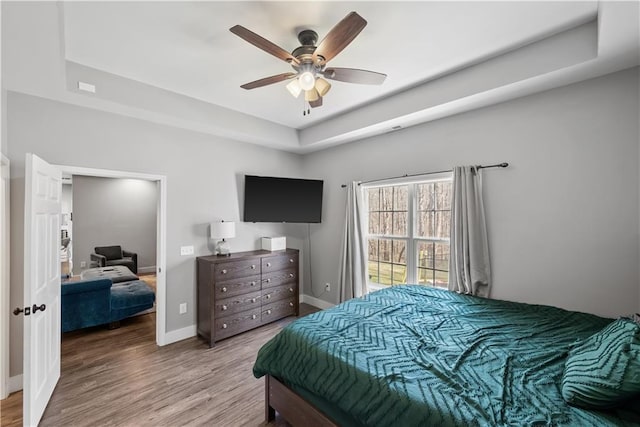 bedroom featuring a ceiling fan, a raised ceiling, wood finished floors, and baseboards