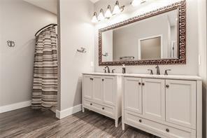 full bath featuring double vanity, wood finished floors, baseboards, and a sink