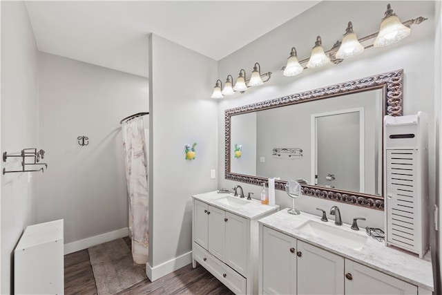 full bathroom featuring wood finished floors, two vanities, baseboards, and a sink