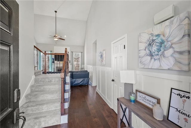 hall with a wall unit AC, stairway, wood finished floors, high vaulted ceiling, and wainscoting