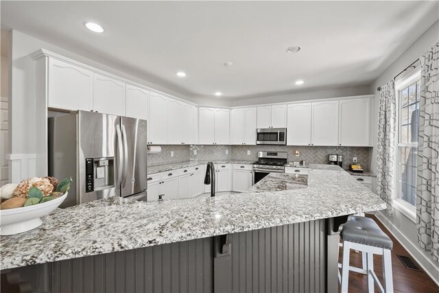 kitchen featuring a breakfast bar, light stone counters, tasteful backsplash, and stainless steel appliances