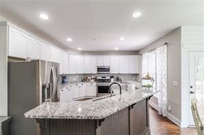 kitchen with a kitchen bar, light stone counters, white cabinetry, appliances with stainless steel finishes, and a large island with sink