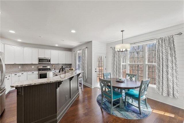 kitchen featuring light stone countertops, decorative backsplash, stainless steel appliances, white cabinetry, and dark wood-style flooring