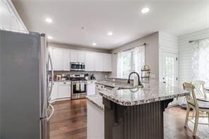 kitchen featuring light stone countertops, a breakfast bar, appliances with stainless steel finishes, white cabinetry, and dark wood-style flooring