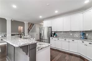 kitchen featuring a spacious island, a breakfast bar, stainless steel refrigerator with ice dispenser, dark wood-style floors, and ornate columns