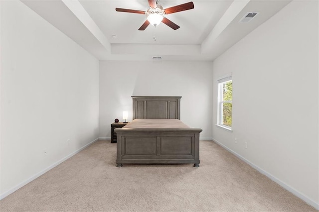 carpeted bedroom with ceiling fan and a tray ceiling