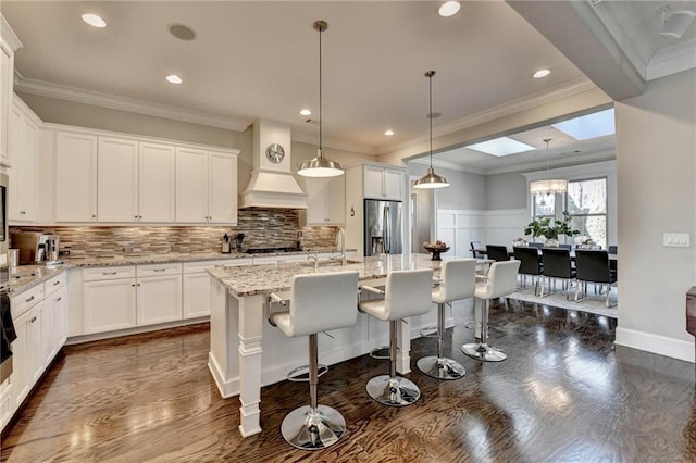 kitchen with white cabinetry, decorative light fixtures, stainless steel fridge, and a center island with sink