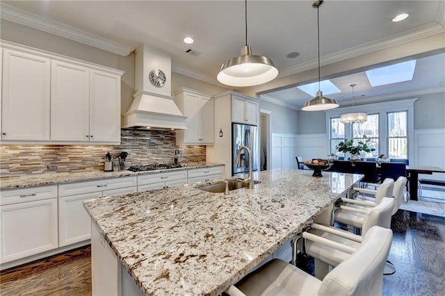 kitchen featuring a kitchen bar, white cabinetry, hanging light fixtures, an island with sink, and stainless steel appliances