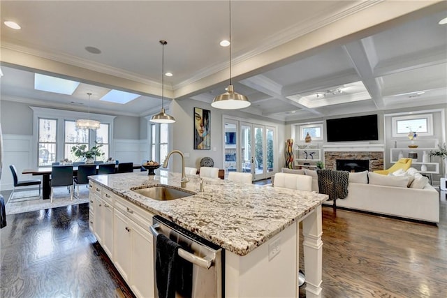 kitchen featuring decorative light fixtures, stainless steel dishwasher, light stone countertops, a kitchen island with sink, and white cabinets