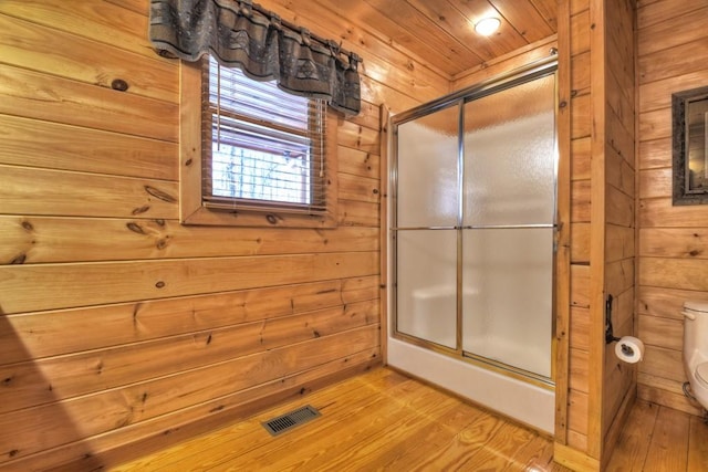 bathroom featuring hardwood / wood-style floors, wood walls, toilet, and an enclosed shower