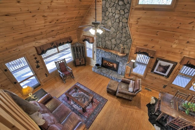 living room with high vaulted ceiling, a stone fireplace, wooden walls, hardwood / wood-style flooring, and ceiling fan