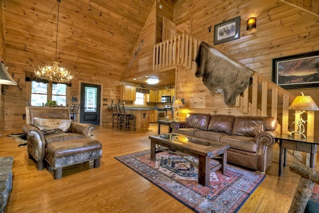 living room with wooden walls, light wood-type flooring, high vaulted ceiling, and an inviting chandelier