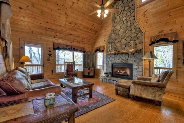 living room featuring a fireplace, light hardwood / wood-style floors, high vaulted ceiling, and wood walls