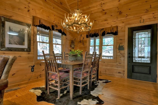 dining room with hardwood / wood-style floors, an inviting chandelier, lofted ceiling, and wood walls