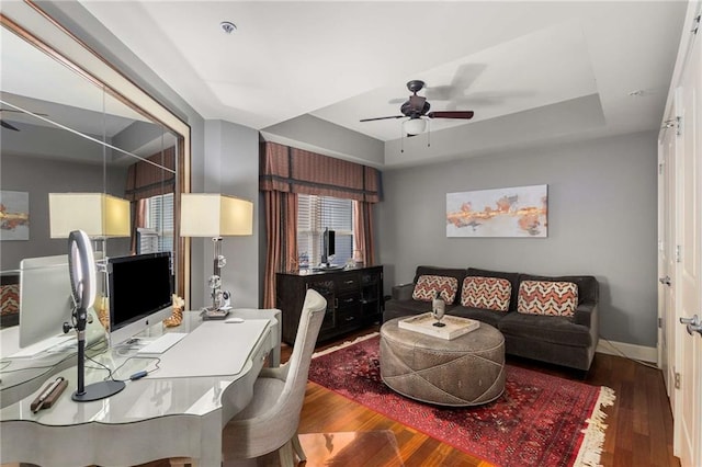 office space featuring a tray ceiling, dark wood-type flooring, and ceiling fan