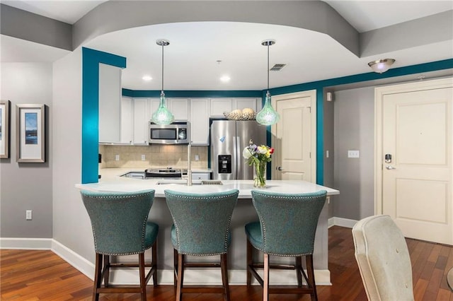 kitchen featuring white cabinets, decorative backsplash, hanging light fixtures, kitchen peninsula, and stainless steel appliances