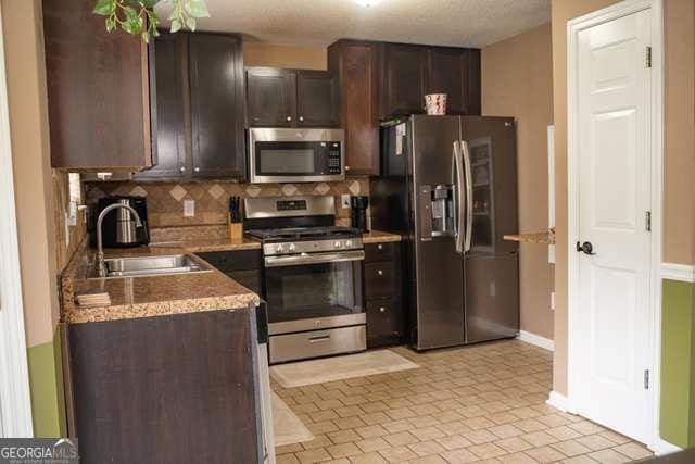 3269 N Winds Trl N, Douglasville, GA 30135 - kitchen featuring stainless steel appliances, a sink, tasteful backsplash, dark brown cabinets, and baseboards