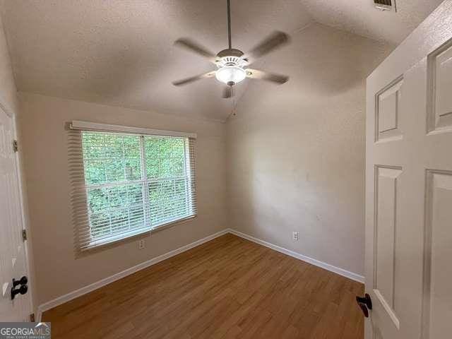 3269 N Winds Trl N, Douglasville, GA 30135 - unfurnished bedroom with lofted ceiling, wood finished floors, baseboards, a ceiling fan, and a textured ceiling