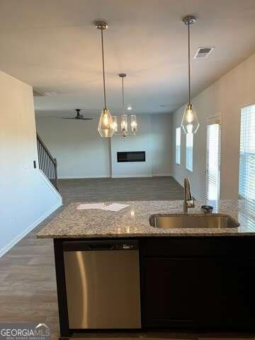 kitchen featuring light stone countertops, stainless steel dishwasher, ceiling fan, sink, and pendant lighting