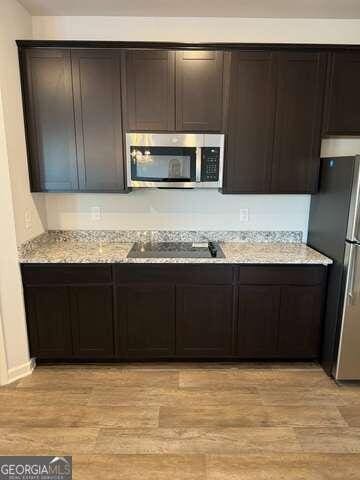 kitchen with dark brown cabinets, light hardwood / wood-style floors, light stone counters, and stainless steel appliances