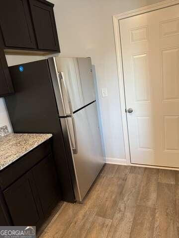 kitchen with light stone countertops, stainless steel fridge, dark brown cabinetry, and light hardwood / wood-style flooring