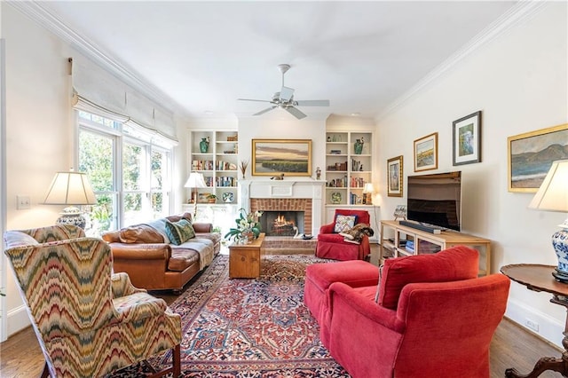 living area with built in shelves, a fireplace, wood finished floors, baseboards, and crown molding