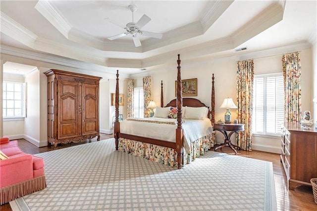 bedroom featuring ornamental molding, a tray ceiling, multiple windows, and wood finished floors