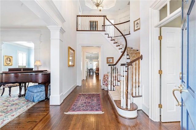 foyer with ornamental molding, stairs, ornate columns, and wood finished floors