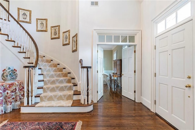 foyer featuring a towering ceiling, stairway, wood finished floors, and visible vents