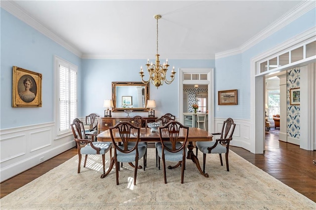 dining room featuring a notable chandelier, crown molding, wood finished floors, and wainscoting