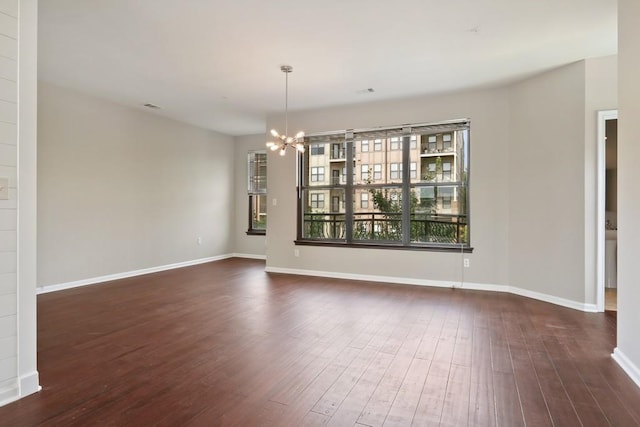 empty room featuring dark wood-type flooring and an inviting chandelier