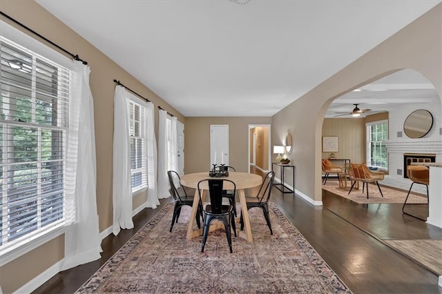 dining room with beamed ceiling, dark hardwood / wood-style flooring, a brick fireplace, and ceiling fan