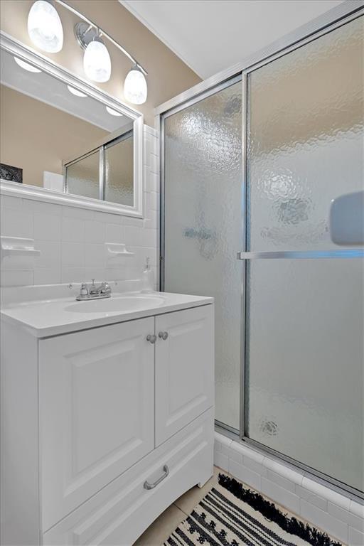 bathroom with tile patterned flooring, vanity, walk in shower, and tasteful backsplash