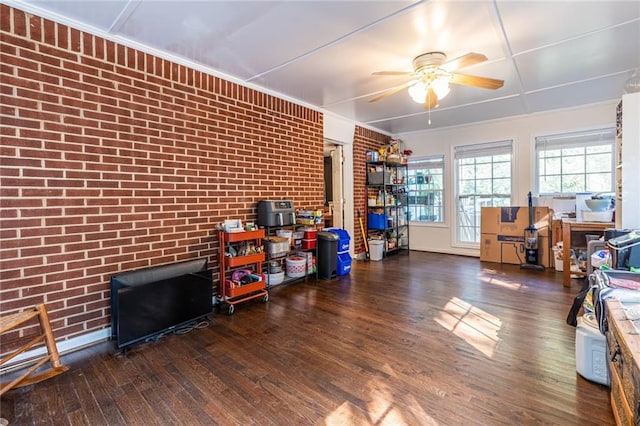 miscellaneous room featuring ceiling fan, dark wood-type flooring, and brick wall