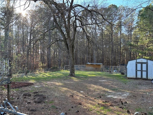 view of yard featuring an outdoor structure, a forest view, fence, and a storage shed