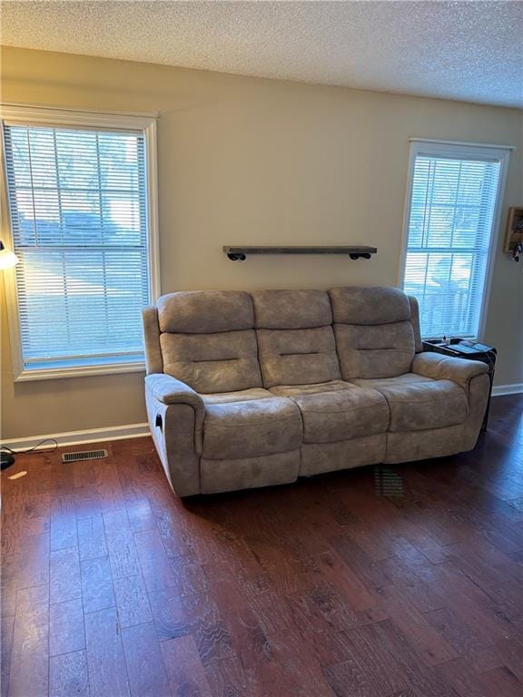 living room featuring baseboards, wood-type flooring, visible vents, and a textured ceiling